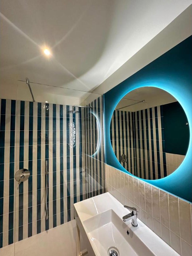 Bagno con piastrelle a righe e specchio tondo illuminato